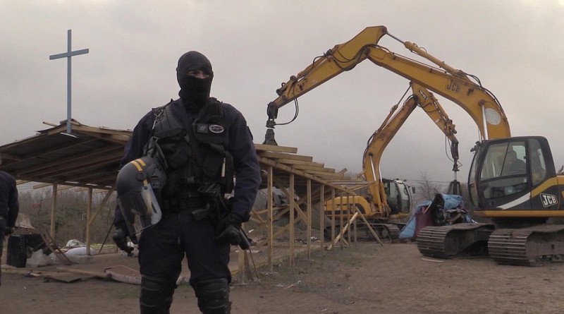 In this frame grab from APTN taken on Monday Feb. 1, 2016, a policeman stands guard as a mechanical digger destroys a makeshift church at a migrant camp in Calais, France. A regional official said the operation Monday was the culmination of a two-week effort to clear a 100-meter security zone around the perimeter of the camp. The official said authorities the migrants and charity groups helping them were informed Jan. 19 of the pending demolition, and that no one was hurt in the operation. (AP Photo/APTN)
